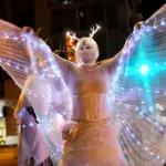 A performer, dressed in whilte, illumated with tiny lights, extends wings at Winter Solstice at Corktown Park